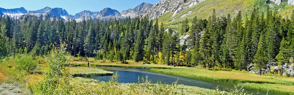 A lone angler fishes beside a small high-country lake beneath the Sierra Nevada.